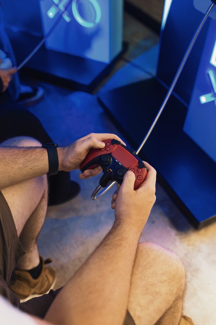 Close-up of a person holding a red gaming controller while playing on a console.